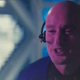 Owen Wilson depicting Jeff Bezos on SNL is purple-hued and wearing a headset with microphone on a spaceship.